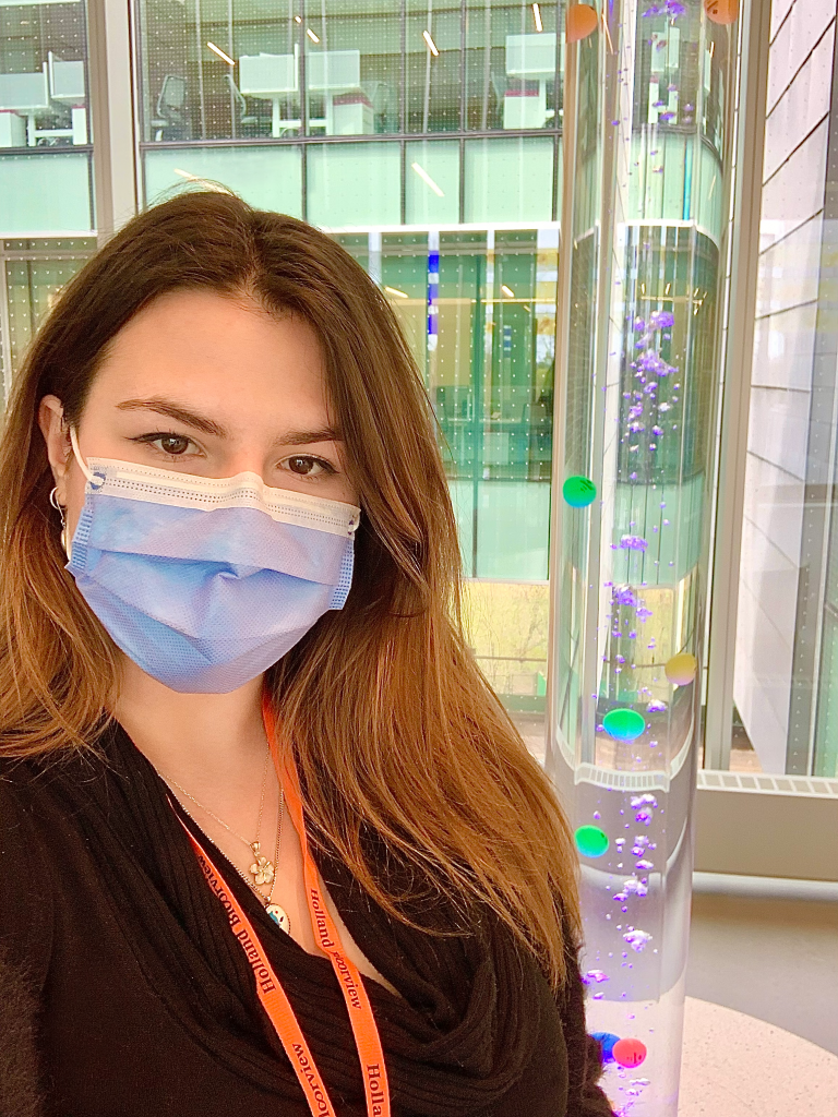 Woman with brown hair, wearing a blue facemask. She is wearing a orange "Holland Bloorview" lanyard. 